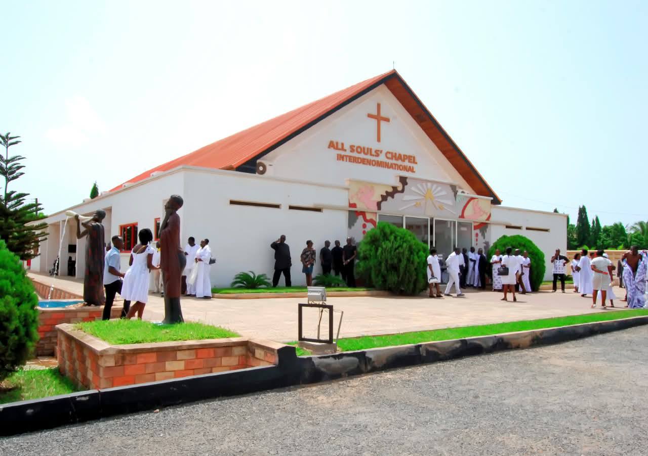 Exterior perspective of All Souls' Chapel Interdenominational at Lashibi Funeral Home under clear skies, welcoming morning guests and family members to the solemn service.