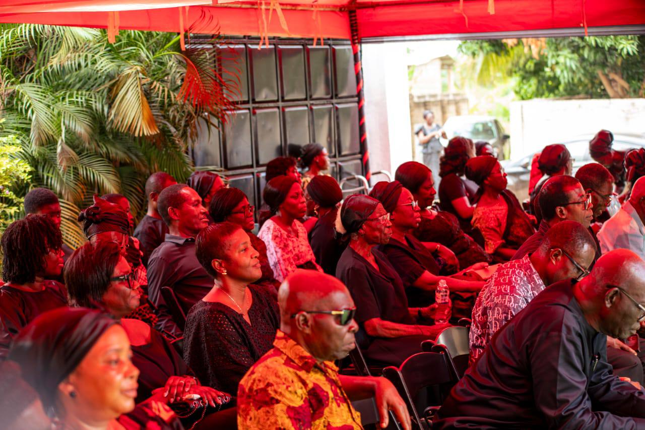 A solemn assembly of extended family, friends, and sympathizers seated under the red and black canopy drapery during the remembrance rites.