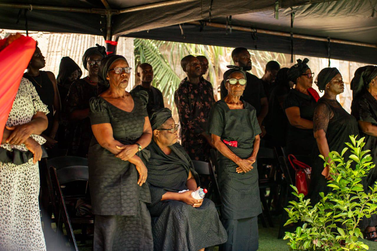 The bereaved widow, matriarchs, and chief mourners standing in traditional black memorial mourning cloths during prayers and songs.